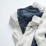 Stylish flat lay featuring denim jeans, white sweater, and eyeglasses on a bright background.